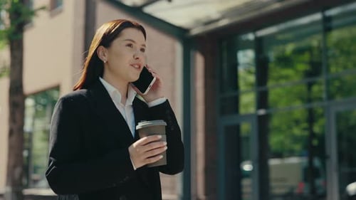 Smiled Businesswoman in Formal Suit Going Near the Business Centre Speaking on the Phone with