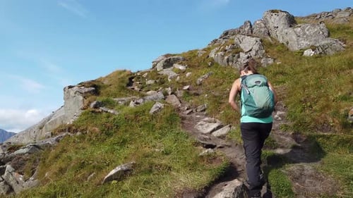 A young brunette woman is walking with her hiking boots and backpack on a trail leading up to the pe