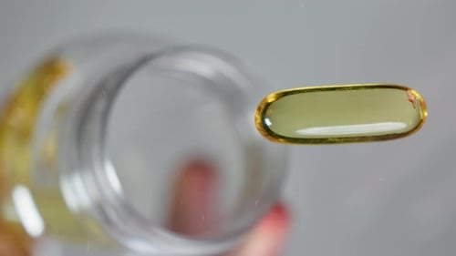 Close up shot hand pouring omega 3 fish oil capsules vitamine D3 vitamin E capsules on flat surface