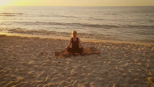 Adult Woman Sitting on Yoga Mat Doing Warm Up Exercises Outside Meditation at Sunset Beach Aerial