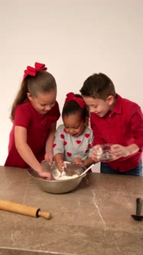 Fröhliche Latino-Kinderbrüder in roten Kleidern stellen auf dem Tisch rollende Butterteller her