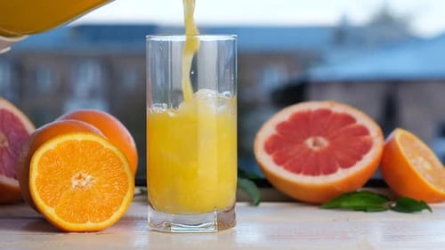 Slowmotion Pour of Citrus Cocktail with Pulp Into a Glass with Ice Cubes Refreshing Juice Made From