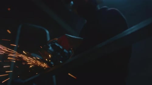 Adult Male Cutting Metal with Sparks in Dark Workplace