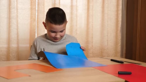 Child Cutting Shapes Out of Paper at Table