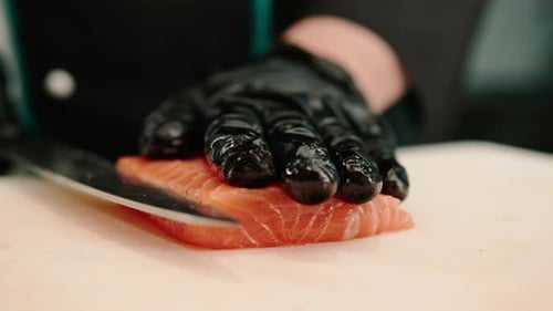 Close-up of a sushi chef cutting a salmon fillet with a knife while preparing sushi in the kitchen