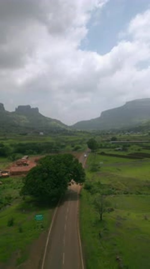 Vue par drone d'une voiture sur l'autoroute Nashik-Trimbak, entourée de verdure luxuriante, de montagnes et de ciel nuageux