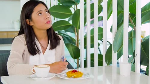 Mujer asiática sonriente disfruta de café y pastel mientras escribe en su cuaderno en un café