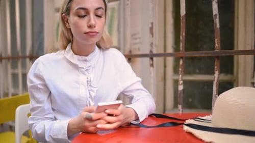 Slow Motion:Attractive young beautiful girl uses smart phone while sitting at a cafe outside.