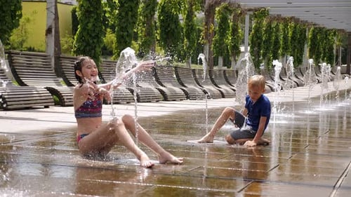 Happy Children Play in the Park with Small Streams of Water in the Fountain