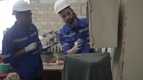 Blue collar workers are working at machine shop with CNC lathe machine.