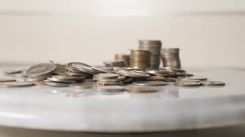 Hand Adjusts Coins on a White Surface