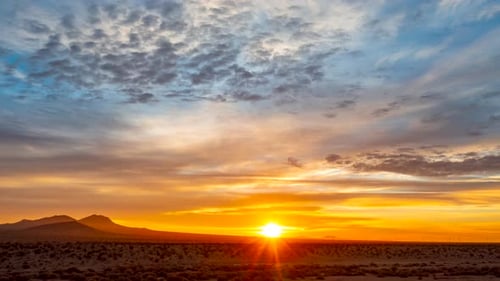 A golden sunrise illuminates the Mojave Desert landscape at dawn with a colorful cloudscape overhead