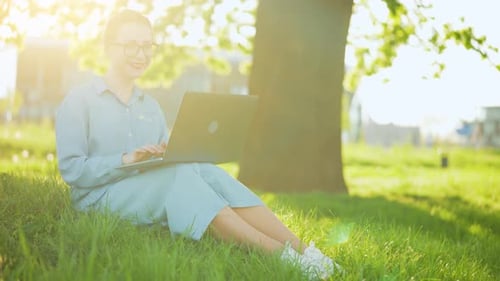 Busy Attractive Woman Working at the Laptop As Sitting on Grass in City Park