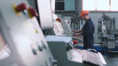 View from the side, working with machine, operator. Factory worker is indoors with hard hat.
