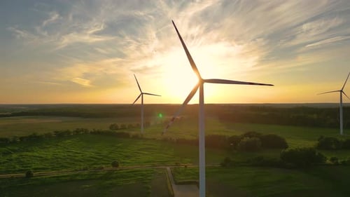 Large wind turbines with blades in field aerial view bright orange sunset blue sky wind park slow mo