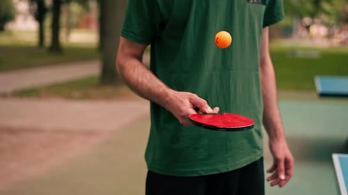 close-up of a man hitting an orange ball with a tennis racket in a city park after playing ping pong