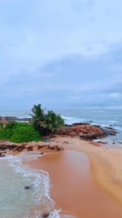 Tranquil scenery of the tropical beach on cloudy day. Ocean waves splash by the coastline. Top view.