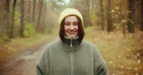 Closeup Portrait of a Happy Young Woman in a Yellow Beanie Smiling at the Camera in an Autumn Forest