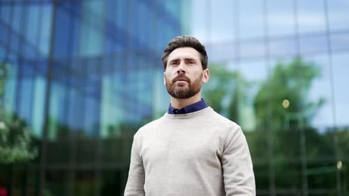 Confident businessman standing near modern glass office building. Professional appearance