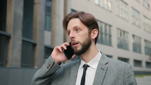 Young Businessman Walking Near an Office Center Talking on the Phone in Slowmotion Male with Beard