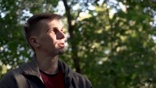 Jeune homme fume une cigarette dans un parc de la ville, portrait en gros plan