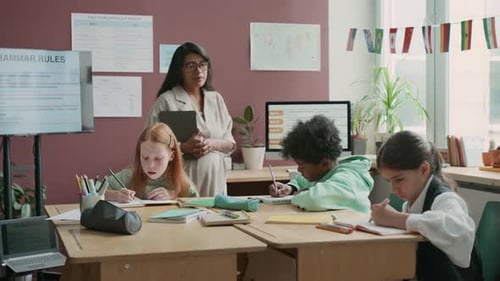 Teacher Helping Elementary Students with Classwork in Classroom