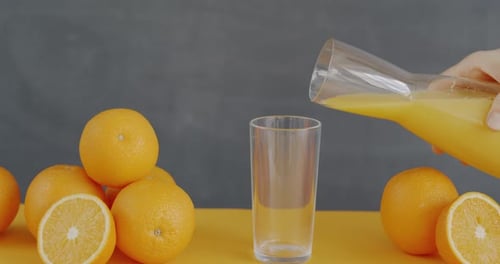 Orange Juice Being Poured into Glass with Oranges