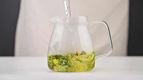 Herbal Tea Preparation: Water Pouring into Glass Pitcher