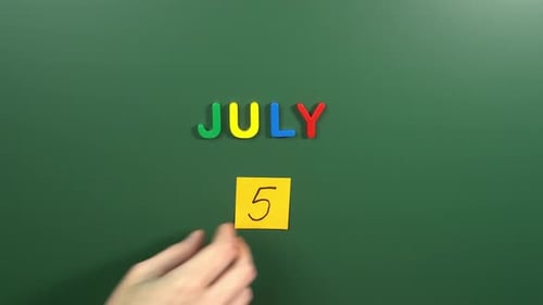 Hand sticking a sticker 5 July calendar day on school board. 5 date of July. Fifth day July