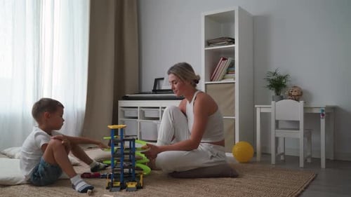 Mother and Her Son Playing Together with a Toy Garage Set on the Floor at Home