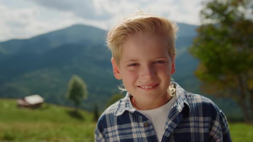 Joyeux garçon blond posant sur un pré vert dans les montagnes pendant les vacances d'été