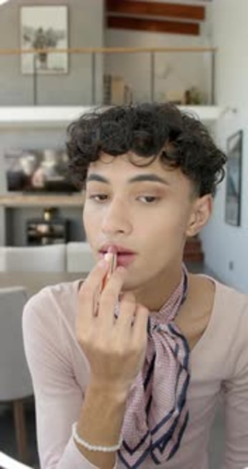 Vertical video: Young person applying lipstick at home, embracing self-expression and confidence