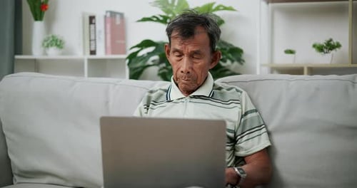 Senior Man Uses Laptop on Couch at Home
