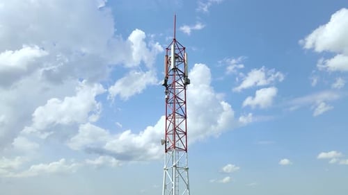 Red and white 5G cell phone tower with blue sky and white clouds in the background