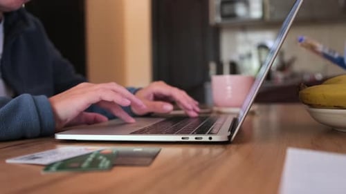 Close up, female hands typing on keyboard laptop lying on wooden table next to bank cards