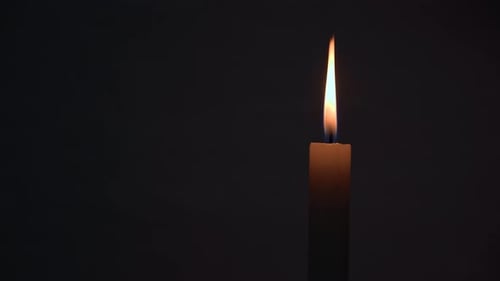 Brightly burning wax candle in the dark on a black background