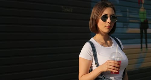 Stylish Woman with Drink Posing in Urban Setting