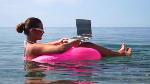 Woman Freelancer Works on Laptop Swimming in Sea on Pink Inflatable Ring Happy Tourist in Sunglasses