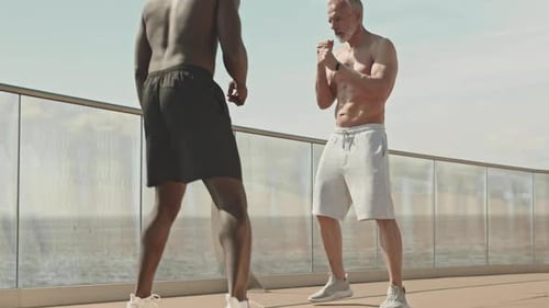 Shirtless Senior Man Practicing Boxing with Trainer Outdoors
