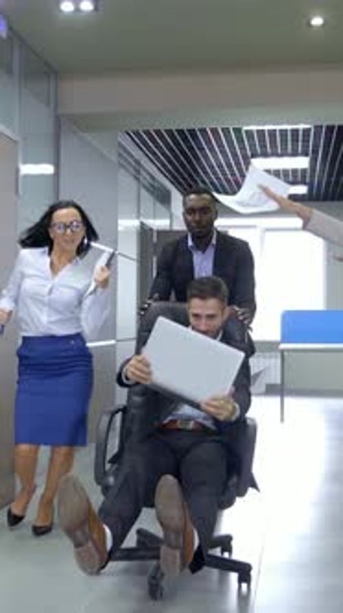 Group of Colleagues Having Fun in Modern Office While One is Being Pushed in a Chair