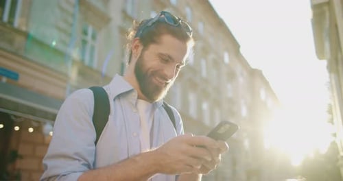 Smiling Man Uses Smartphone in Sunny City