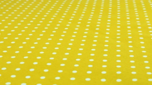 Close-up view of the safety yellow with white polka dots cotton fabric rotated on the display case.