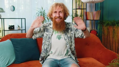 Smiling Man Waving Hello Indoors on Sofa