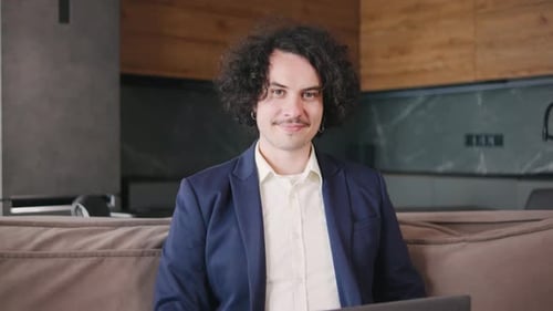 Curly Focused Business Man in a Jacket and Pajama Pants Working on Laptop Sitting at Home Office