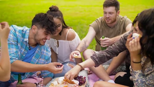 Happy friends enjoying food and drinks together at a summer picnic in the park