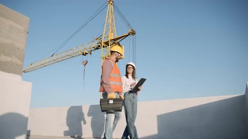 Construction workers collaborate in slow motion on a building site with a crane in the backdrop