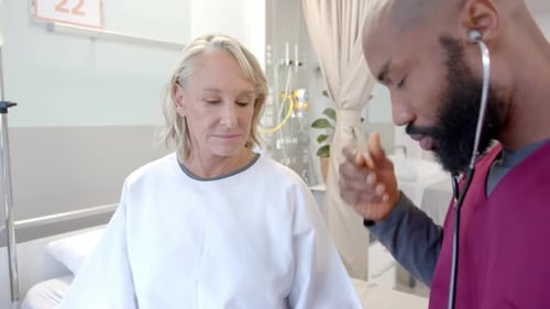 African american male doctor with stethoscope examining caucasian female patient at hospital
