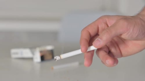 Nahaufnahme einer Hand, die eine brennende Zigarette hält