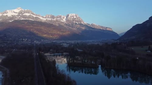 Aerial shot moving towards the town of Sallanches over the train railroad and the lakes, very early