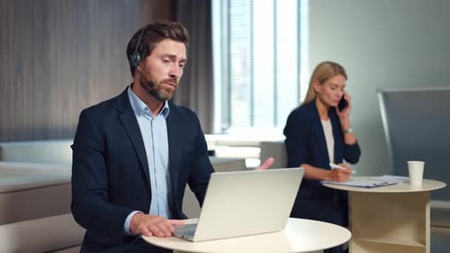 Man in Headset Having Video Chat on Laptop While Woman Talking on Mobile